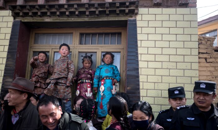 This picture taken on March 1, 2018 shows children in traditional Tibetan clothes and police watching passing Tibetan Buddhist monks during a ceremony for Monlam, otherwise known as the Great Prayer Festival of Losar, the Tibetan New Year, at the Rongwo Monastery, in Tongren County, Huangnan Tibetan Autonomous Prefecture, on the Qinghai-Tibet plateau.  Scores of monks and men heaved the enormous thangka -- an image of Buddha painted on silk, rolled up in a tight cylinder while in transit -- through the packed streets around Rongwo Monastery in China's northwestern province of Qinghai for a religious ritual wrapping up Losar, the Tibetan new year.  / AFP PHOTO / Johannes EISELE        (Photo credit should read JOHANNES EISELE/AFP via Getty Images)